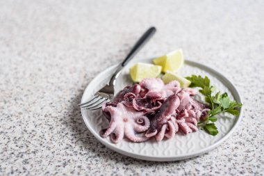 Gri arka planda kireç ve otlar ile gri bir plaka lezzetli bebek ahtapot. Seçici odak