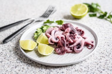 Gri arka planda kireç ve otlar ile gri bir plaka lezzetli bebek ahtapot. Seçici odak