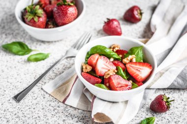 Gri bir arka planda çilek ve fındık ile lezzetli taze ıspanak salata. Çilek ile yaz salatası