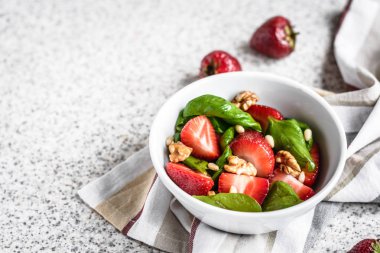 Gri bir arka planda çilek ve fındık ile lezzetli taze ıspanak salata. Çilek ile yaz salatası