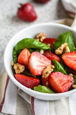 Gri bir arka planda çilek ve fındık ile lezzetli taze ıspanak salata. Çilek ile yaz salatası