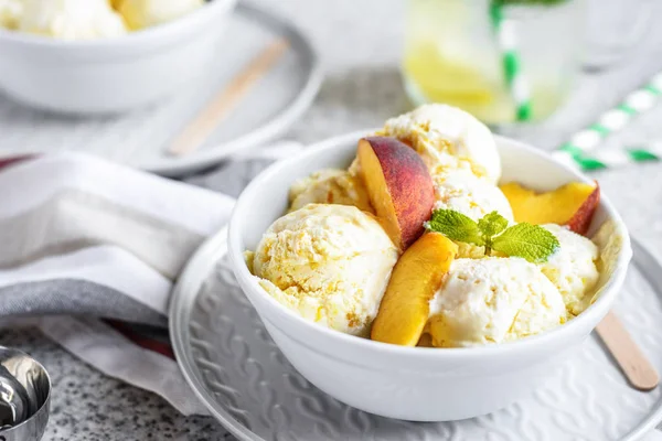 Delicious homemade peach ice cream with mint and fresh peach slices in a plate on a gray background