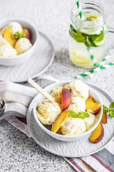 Delicious homemade peach ice cream with mint and fresh peach slices in a plate on a gray background