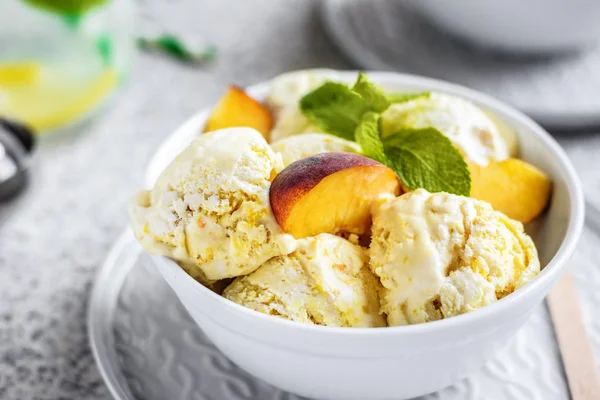 Gri bir arka planda bir plaka nane ve taze şeftali dilimleri ile lezzetli ev yapımı şeftali dondurması