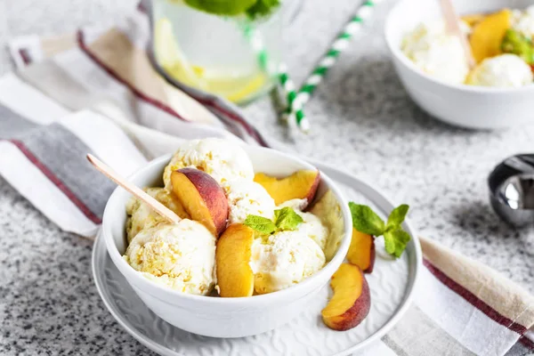 Delicious homemade peach ice cream with mint and fresh peach slices in a plate on a gray background