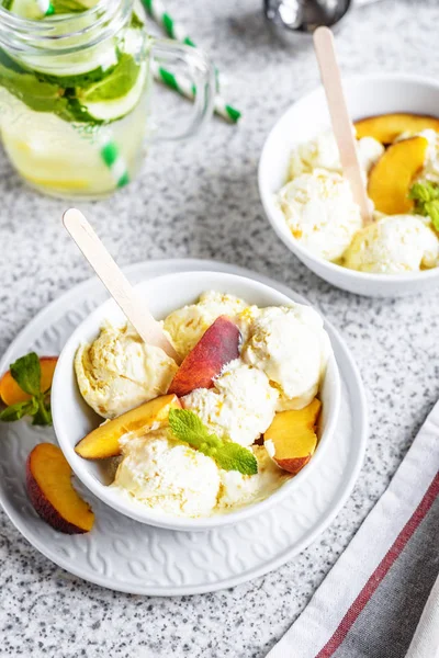 Delicious homemade peach ice cream with mint and fresh peach slices in a plate on a gray background