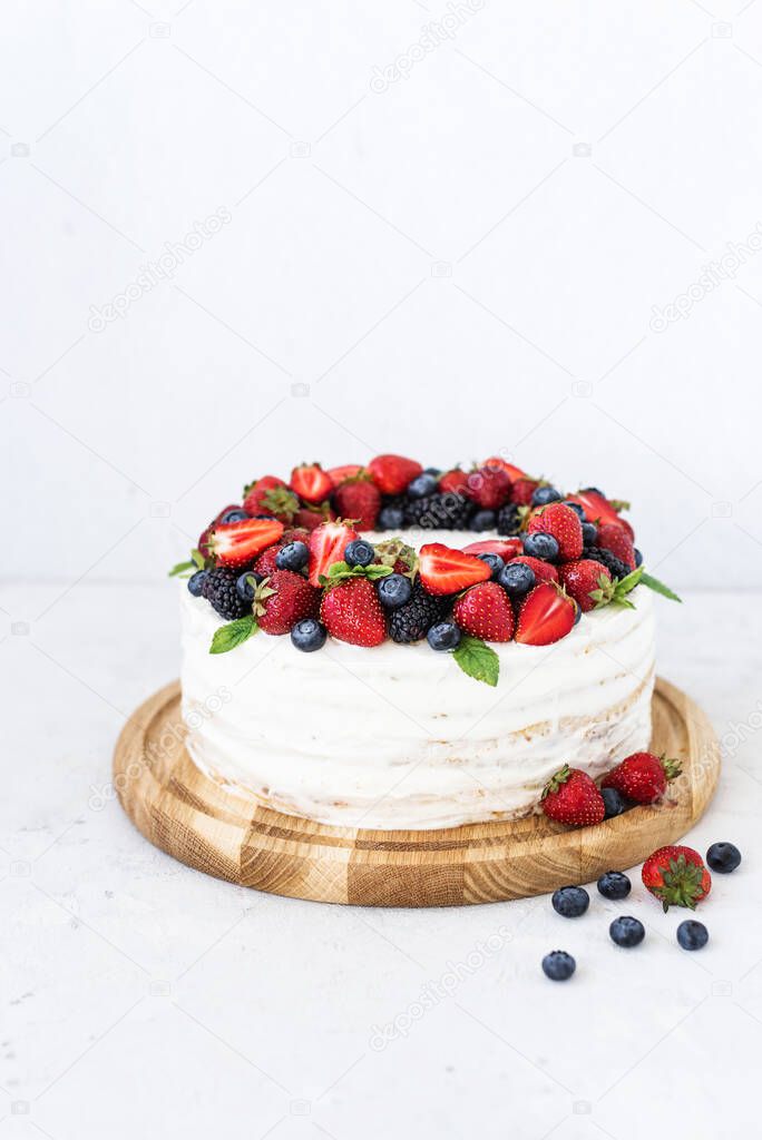 Rustic cake with fresh berries. Delicious fresh cake on a white background. Strawberry cake with blueberries and mint. Homemade blueberry vanilla cream cake