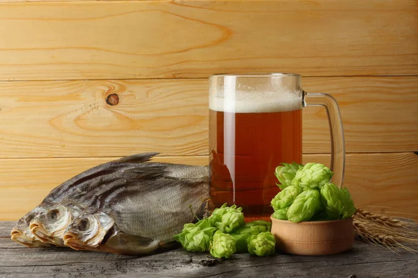 Glass beer with hop cones, dried fish and wheat ears on light wooden background. Beer brewery concept. Beer background