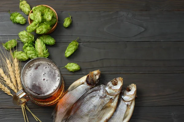 Glass beer with hop cones and dried fish on dark wooden background. Beer brewery concept. Beer background. top view