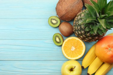 taze Hindistan cevizi, muz, kivi, portakal ve mavi ahşap arka plan üzerinde ananas karışımı. kopya alanı ile üstten görünüm