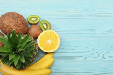 taze Hindistan cevizi, muz, kivi, portakal ve mavi ahşap arka plan üzerinde ananas karışımı. kopya alanı ile üstten görünüm
