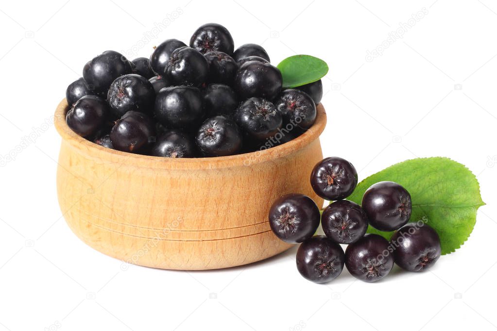 Chokeberry in wooden bowl with green leaves isolated on white background. Black aronia 