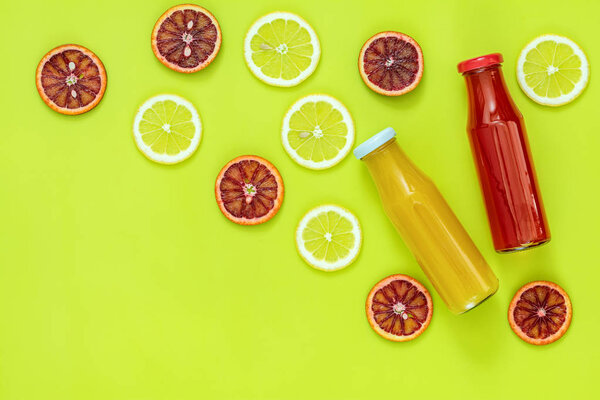 Прекрасный кулинарный фон. Желтый и красный сок в стеклянных бутылках нарезанный лимон и кровь оранжевые фрукты на ярко-зеленой поверхности
.