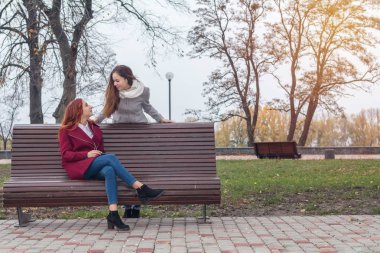 İki mutlu sevimli güzel kadın gençler kürsüye bir sonbahar Şehir Parkı içinde