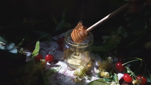 Honig Glas Gießen Lindenblüten Und Rote Kirschen Auf Holzoberfläche Sonnenstrahl — Stockvideo