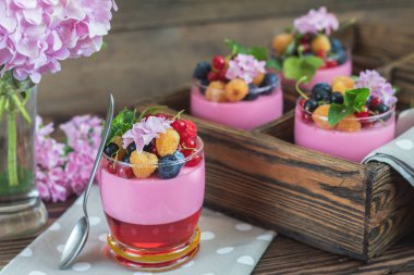 Multivitamin summer berry delicious panacotta. Sweet food with raspberries, blueberries, currants, croutons and mint, pink hydrangea bouquet, dark wooden background. clipart