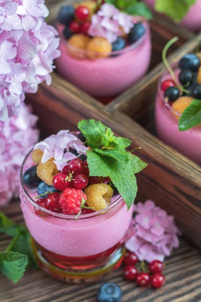 Multivitamin summer berry delicious panacotta. Sweet food with raspberries, blueberries, currants, croutons and mint, pink hydrangea bouquet, dark wooden background.