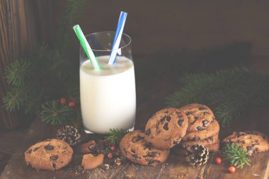 Lezzetli çikolata kurabiye ve bardak süt, çam dalları ve çam kozalakları koyu ahşap arka plan üzerinde Noel ve yeni yıl kompozisyonu.