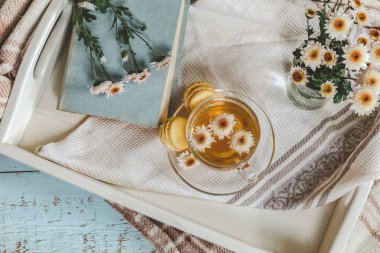 Bir fincan çay, kitap, kasımpatı çiçekleri ve macaroons içinde tepsi masanın üzerinde. Rahat ev concept. Boyama ve sinema tarzı içinde fotoğraf işleme.