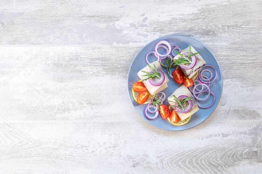 Delicious rolled herring fillet with red onion, cherry tomatoes, lemon and rosemary. Close up, restaurant serving, light gray wooden surface, copy space, top view.