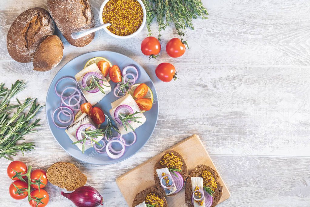 Delicious rolled herring fillet with red onion, cherry tomatoes, lemon and rosemary. Close up, restaurant serving, light gray wooden surface, copy space, top view.