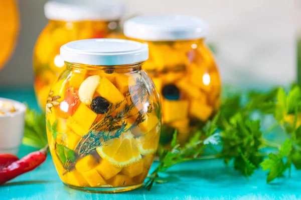 Marinated preserving jars. Homemade orange cut pumpkin pickles with red hot chili peppers, fresh parsley, spices on light turquoise wooden background. Fermented food.