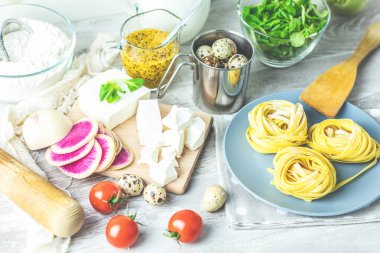 Plaka, bıldırcın yumurtası, yeşil salata, domates, Fransız hardalı, beyaz peynir, dilimlenmiş Kırmızı turp ve un masa lambası üzerinde üzerinde ham ev yapımı İtalyan tipik makarna makarna erişte. Sığ derinlik-in tarla