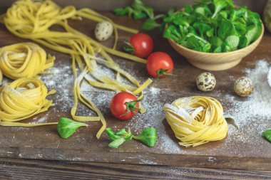 Ham ev yapımı İtalyan tipik Makarna Makarna Erişte, bıldırcın yumurtası, yeşil salata, domates ve un koyu ahşap masa üzerinde. Alan derinliği sığ, yakın çekim, alanı Kopyala.