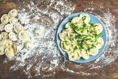 Yukarıdan lezzetli ev yapımı et köfte veya kepekli un plaka üzerinde taze maydanoz ve koyu ahşap masa yüzeyi, kopya alanı, ham Mantı serpilir geleneksel İtalyan Mantısı görüntülemek.