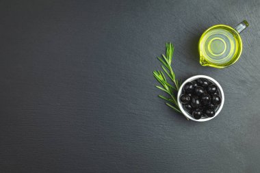 Plaka, zeytin yağı ve biberiye siyah bir taş zemin üzerine siyah zeytin ayarlayın. Metin için boş alan.