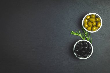 Yeşil ve siyah zeytin plaka üzerinde ve siyah bir taş zemin üzerine biberiye kümesi. Metin için boş alan.