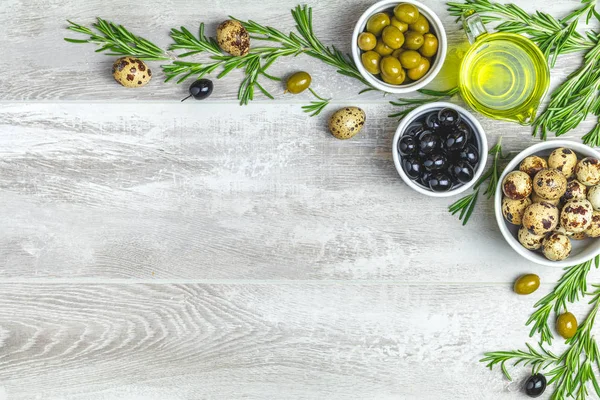 Siyah ve yeşil zeytin ayarla, tabaklar, zeytin yağı ve biberiye, ışık gri ahşap arka plan üzerinde Bıldırcın yumurta. Üstten görünüm, kopya alanı.