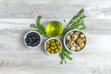 Tabaklar, zeytin yağı ve biberiye ışık gri ahşap arka plan üzerinde siyah ve yeşil zeytin ayarlayın. Üstten görünüm, kopya alanı.