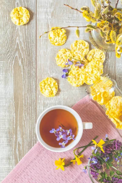 すみれ色のビオラ おいしい栄養価の高い穀物パン 木製のテーブルの春の花とお茶のカップ 栄養価の高い朝食 平面図 コピー スペース — ストック写真