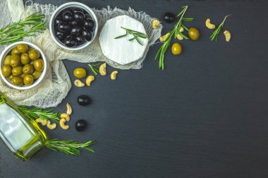 Peynir camembert, siyah ve yeşil zeytin, bıldırcın yumurtası plakaları, zeytin yağı ve biberiye, siyah taş tablo arka plan üzerinde kümesi. Üstten görünüm, kopya alanı.