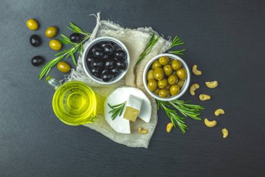 Peynir camembert, siyah ve yeşil zeytin, bıldırcın yumurtası plakaları, zeytin yağı ve biberiye, siyah taş tablo arka plan üzerinde kümesi. Üstten görünüm, kopya alanı.