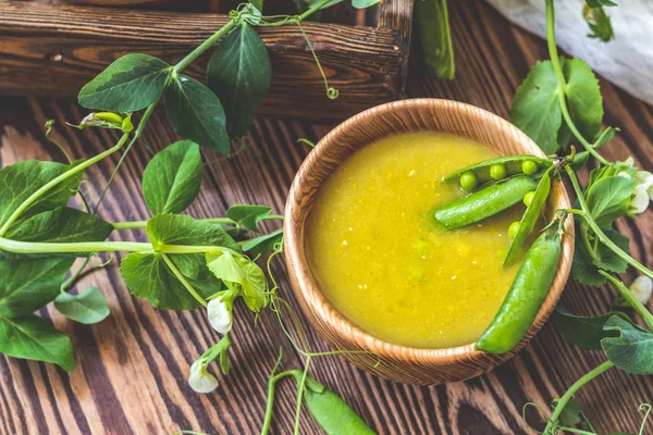 Wooden plate of pea soup and pods of fresh green peas on a dark wooden surface. Vintage wooden surface for design with beautifully located pods of green peas. Shallow depth of field.