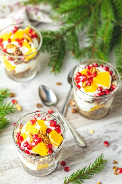 Greek yogurt with granola, orange and pomegranate berries for healthy breakfast on light gray wooden table, copy space, shallow depth of the field.