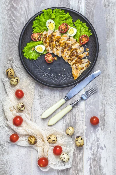 Delicious salad, chicken with honey and mustard souse, lettuce, quail eggs, cherry tomatoes and sesame in black ceramic plate, top view, copy space, hawaiian, asian food