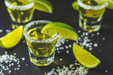 Meksika altın tekila kireç ile vurdu ve tuz siyah taş masa yüzeyi, seçici odak, sığ derinlik-in tarla, kopya alanı.