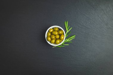 Plaka üzerinde yeşil zeytin ve siyah bir taş zemin üzerine biberiye kümesi. Metin için boş alan.