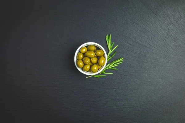 Plaka üzerinde yeşil zeytin ve siyah bir taş zemin üzerine biberiye kümesi. Metin için boş alan.