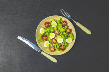 Taze sağlıklı salata marul, bıldırcın yumurtası, kiraz domates ve susam plaka ile. Üstten görünüm, kopya alanı, siyah taş yüzey.