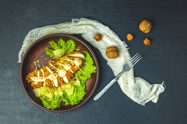 Delicious salad, chicken with pineapple, lettuce, cream sauce and walnut in ceramic plate on blackstone surface, top view, copy space, hawaiian, asian food