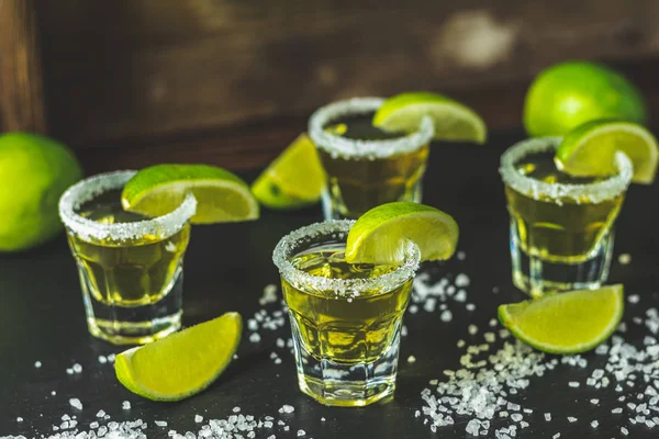 Mexican Gold Tequila shot with lime and salt on black stone table surface, selective focus, shallow depth of the field, copy space.