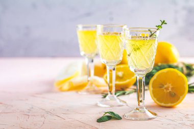 Geleneksel İtalyan ev yapımı limon alkol içki likör limoncello adet limon ve biberiye bitki hafif pembe mercan taş beton yüzeyine yaşayan üzerinde