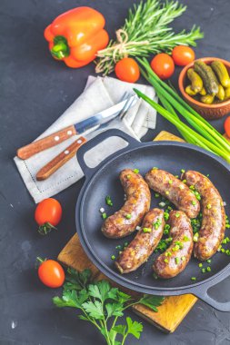 Otlar ve baharatlar ile bir tavada kızarmış sosis. Bir ahşap tahta üzerinde bıçak ve çatal, hardal, yeşil soğan, maydanoz ve salatalık turşusu ile servis edilir, metniniz için boş.