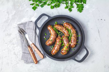 Bıçak ve çatal, yeşil soğan, maydanoz ve biberiye açık gri beton yüzey arka plan, üst görünüm, metin için boş alan ile otlar ve baharatlar ile bir tavada kızarmış sosis.