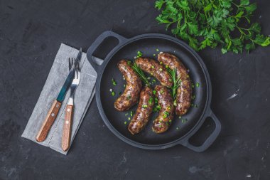 Otlar ve baharatlar ile bir tavada kızarmış sosis. Taş bir gemide hizmet bıçak ve çatal, maydanoz, metniniz için boş alan ile.
