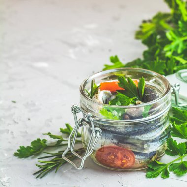 Sardalye veya biberiye, kekik, maydanoz, domates dilimleri ve boşluk cam hafif gri beton masa yüzeyi ile Baltık Ringa balığı. Marine Deniz balığı korunmuş, sizin metin için yer kopyalayın.